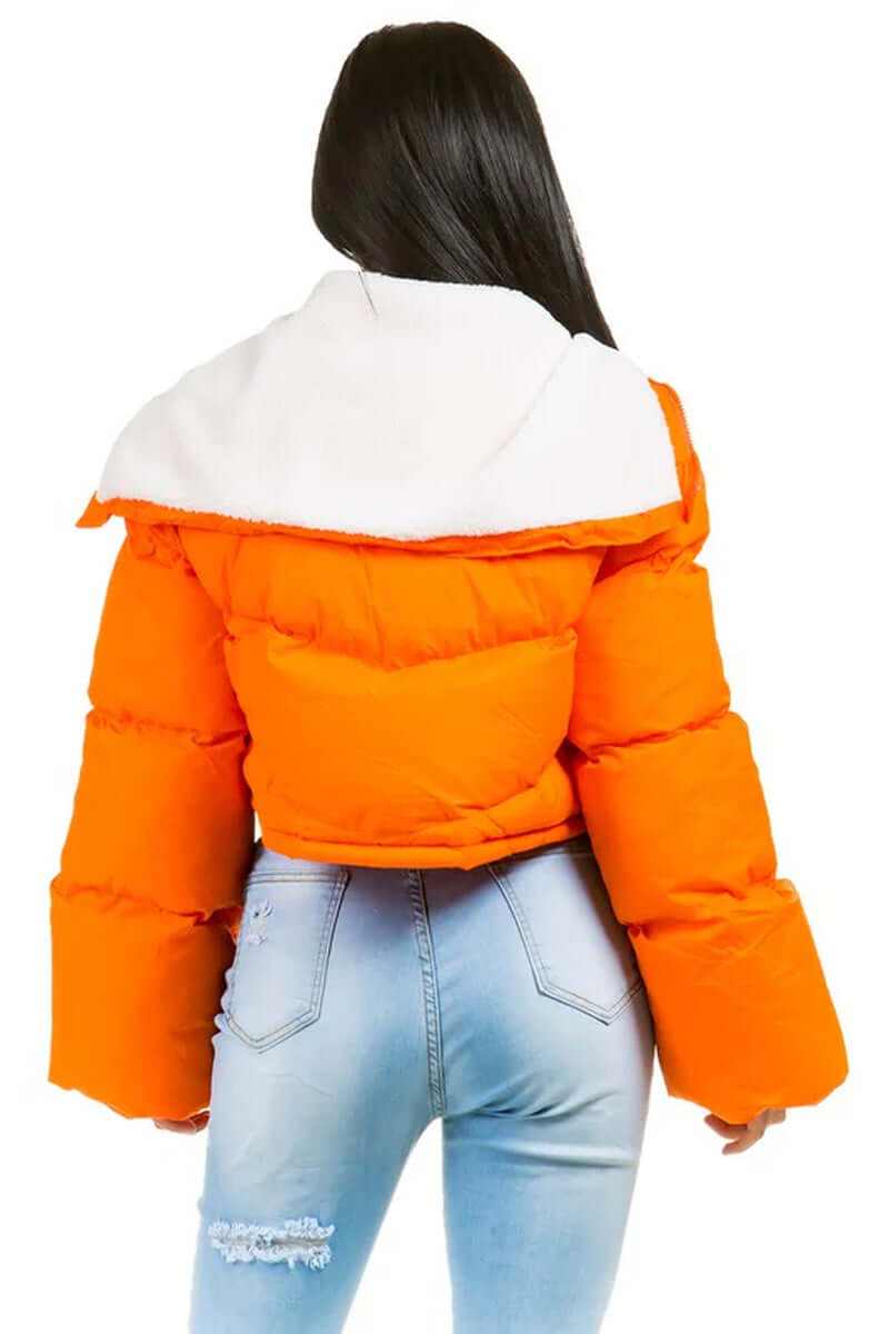 Back view of a women's orange fuzzy teddy puffer jacket with white collar and oversized sleeves paired with jeans.