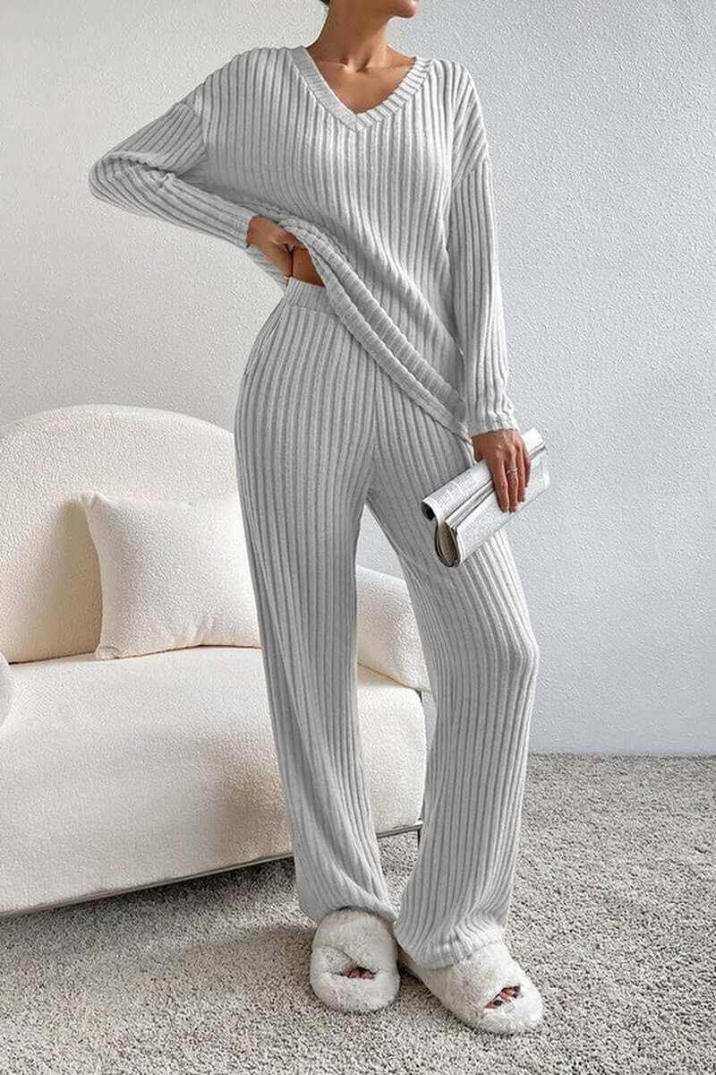Women wearing a grey ribbed knit slouchy two-piece outfit with a V-neck design, styled with a clutch and slippers.