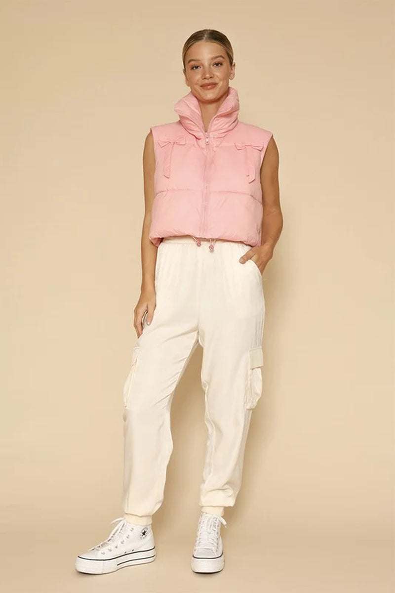 Woman wearing pink cropped puffer vest with bow detail and white pants