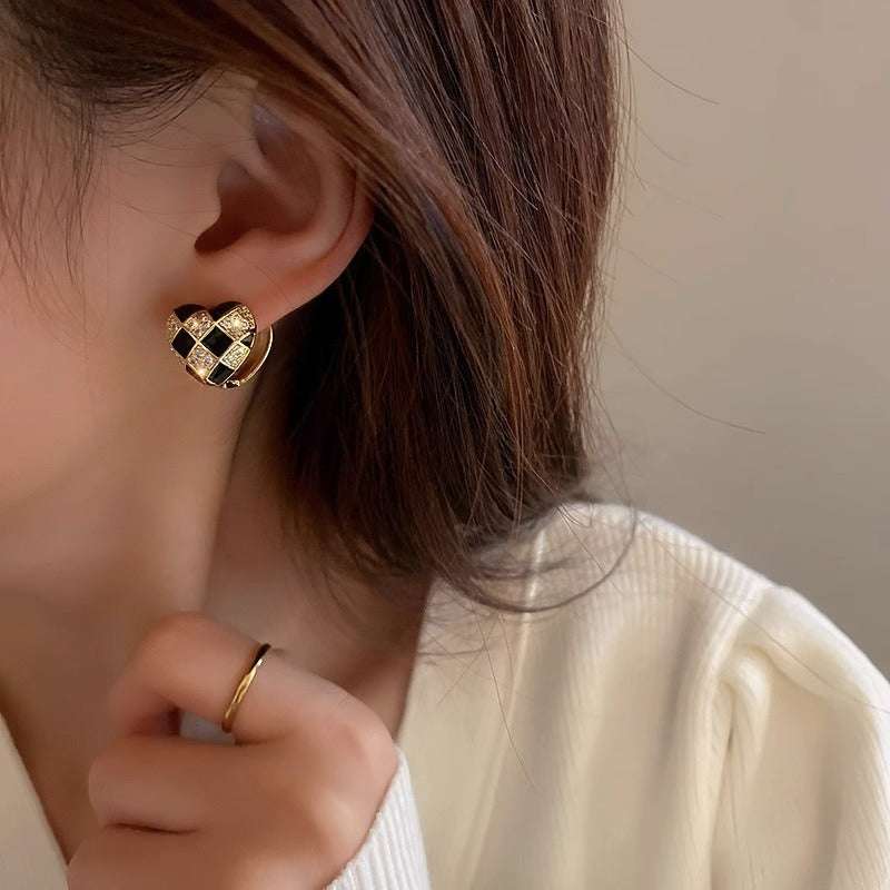 Close-up of ear wearing heart-shaped plaid black and gold stud earring with copper electroplated finish