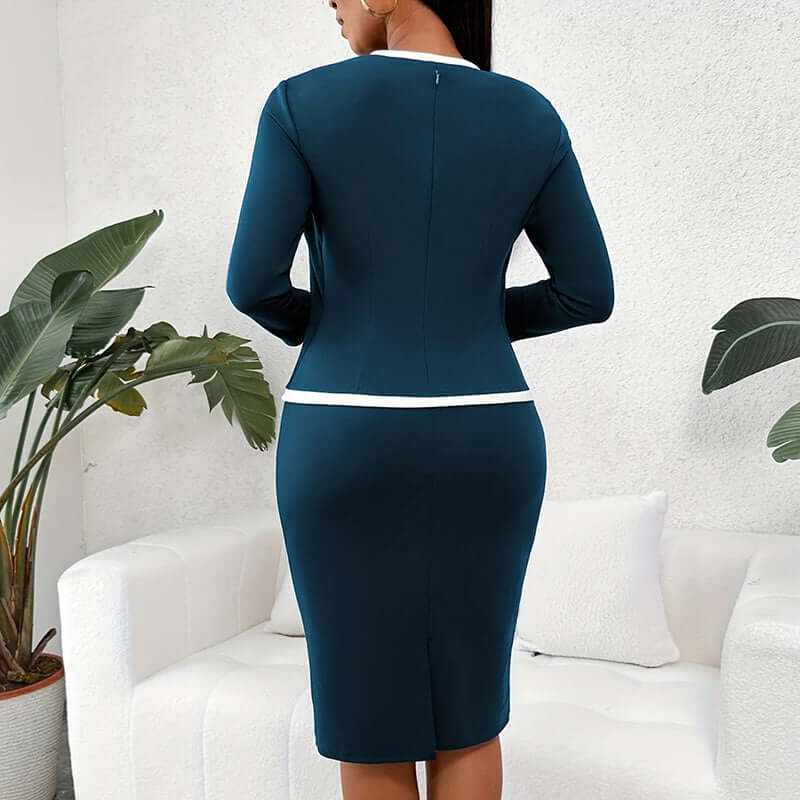 Woman wearing navy blue mock two-piece office dress with white trim, standing indoors near plants and white sofa, back view