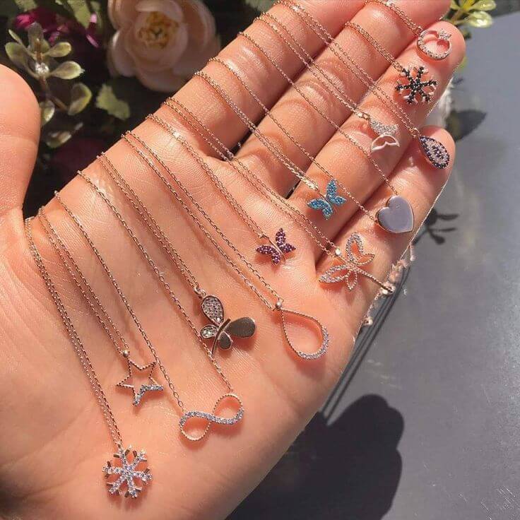 Hand displaying an array of delicate fashion jewelry necklaces with unique pendants, including butterflies and stars.