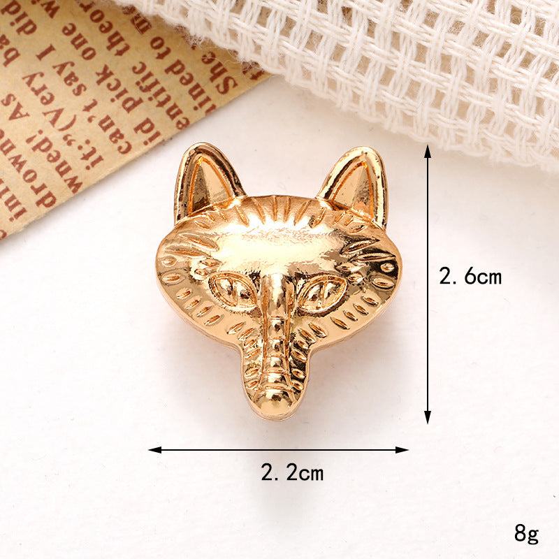 Gold fox head brooch with detailed features and measurements on a patterned background.