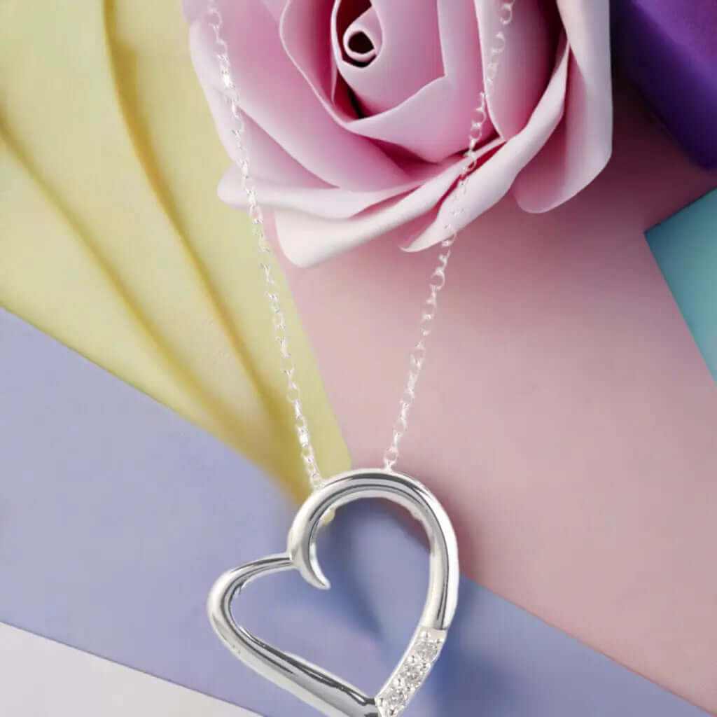 14K silver plated love heart pave pendant necklace resting on colorful background with rose.