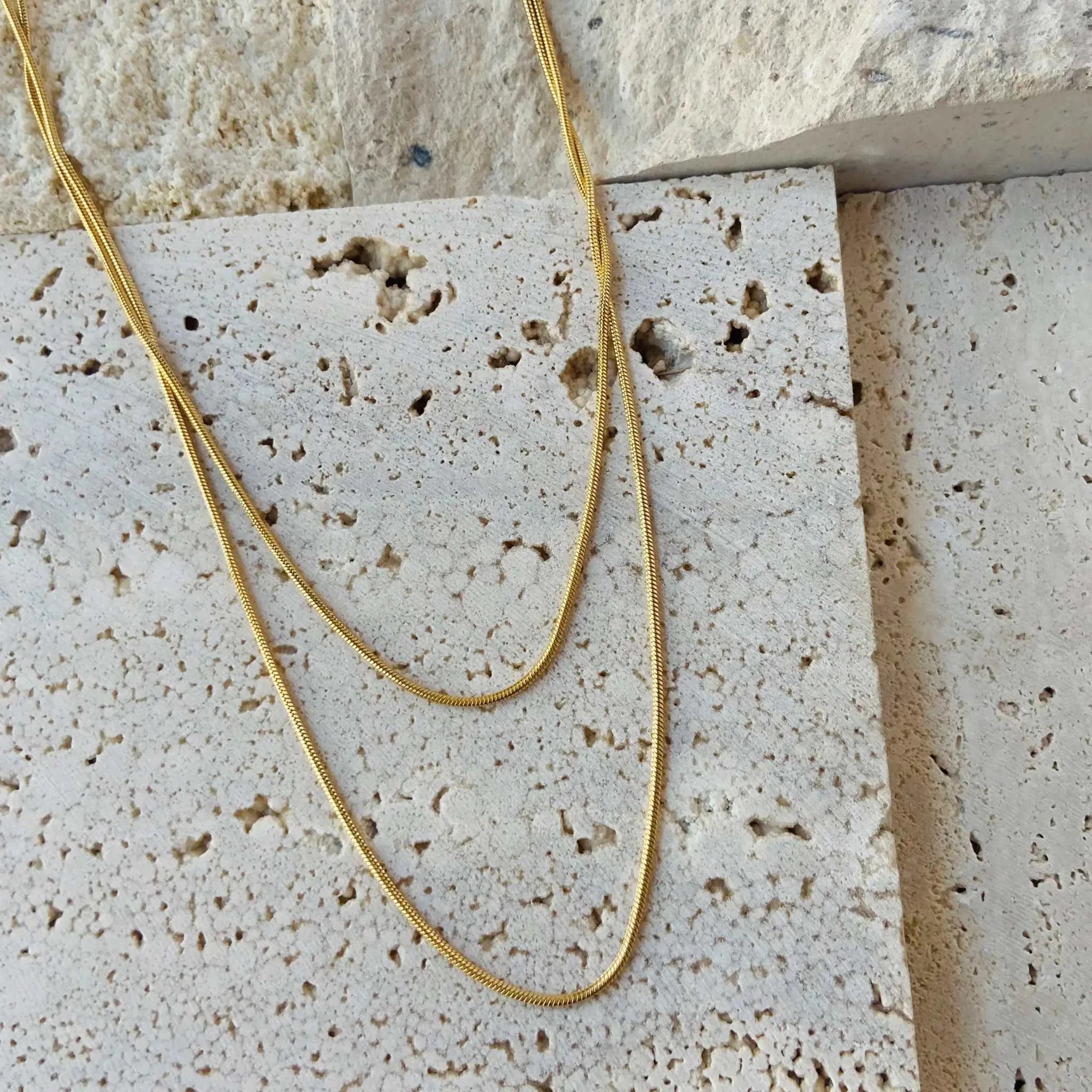 18K gold plated double-row snake chain necklace displayed on textured stone background.