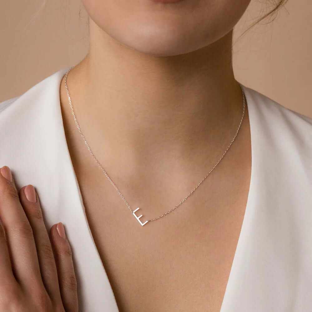 Close-up of a woman wearing a sideways initial letter necklace in silver, complementing her elegant outfit.
