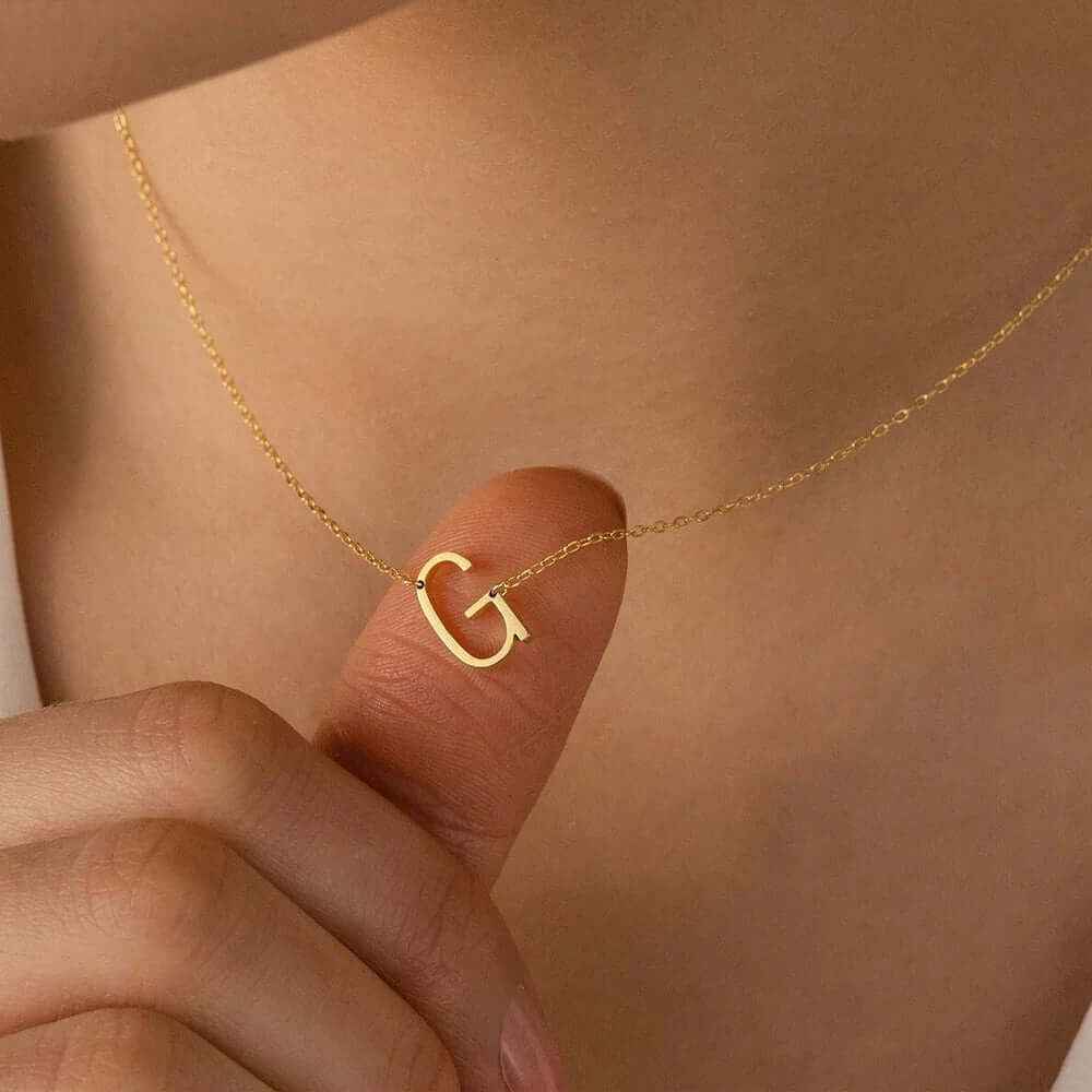 Close-up of a person holding a sideways initial letter 'G' necklace in 18k gold plating.