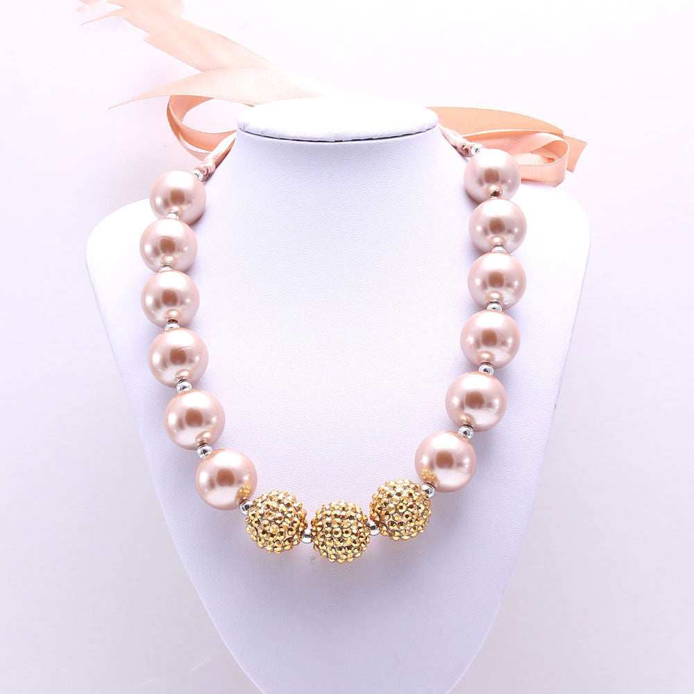 European style children's pearl necklace with large pink beads and three gold decorative spheres on white display bust