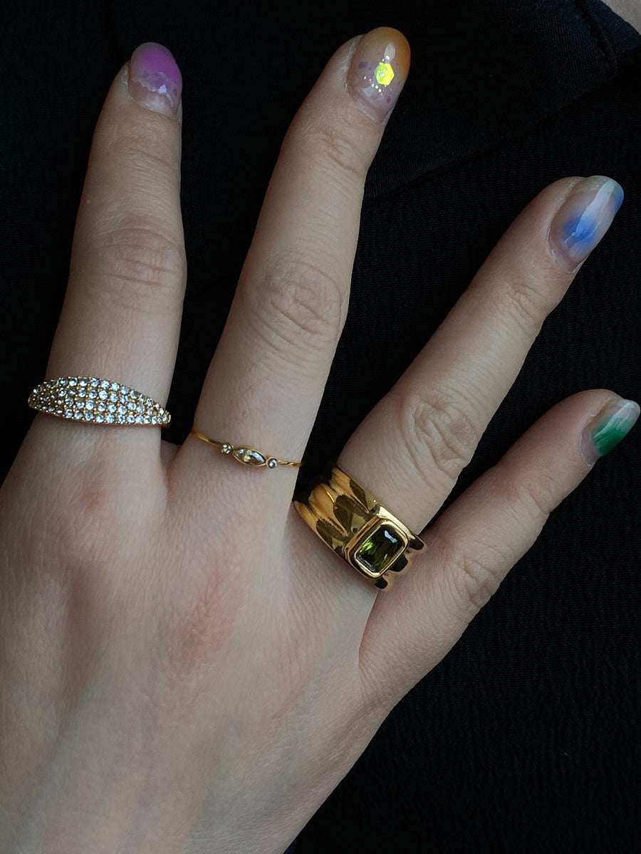 hand wearing delicate candy-colored pearl statement ring with gold and silver plated designs on black background