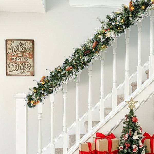 pre-lit snow flocked Christmas garland decorating a staircase with holiday decorations and a Christmas tree.