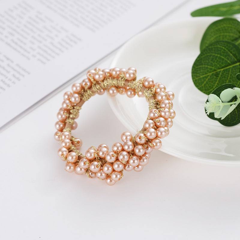 Beaded hair rope made of cloth with clustered pink pearls on a white surface with green leaves background