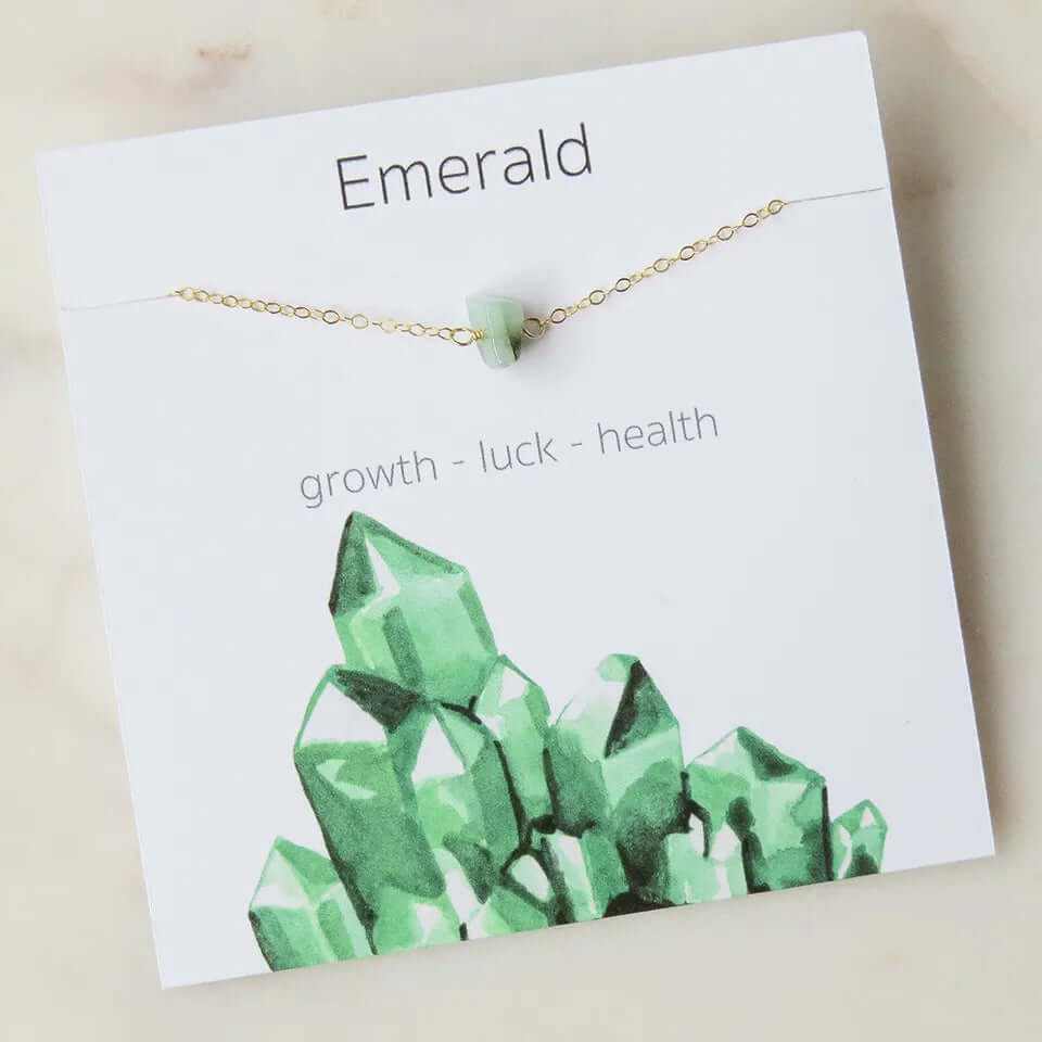 Emerald charm pendant necklace displayed on card, symbolizing growth, luck, and health with geometric design.