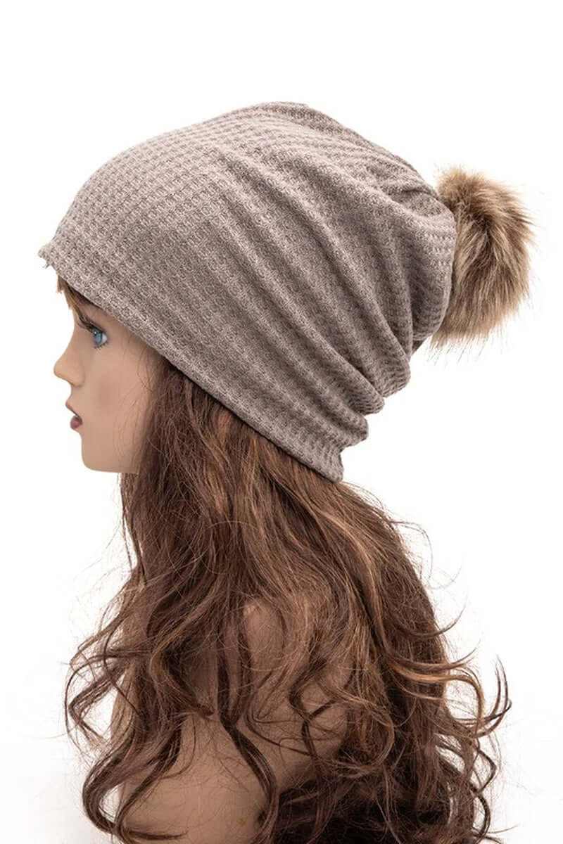 Profile view of a cotton slouchy beanie with faux pom in taupe, perfect for cold-weather fashion.