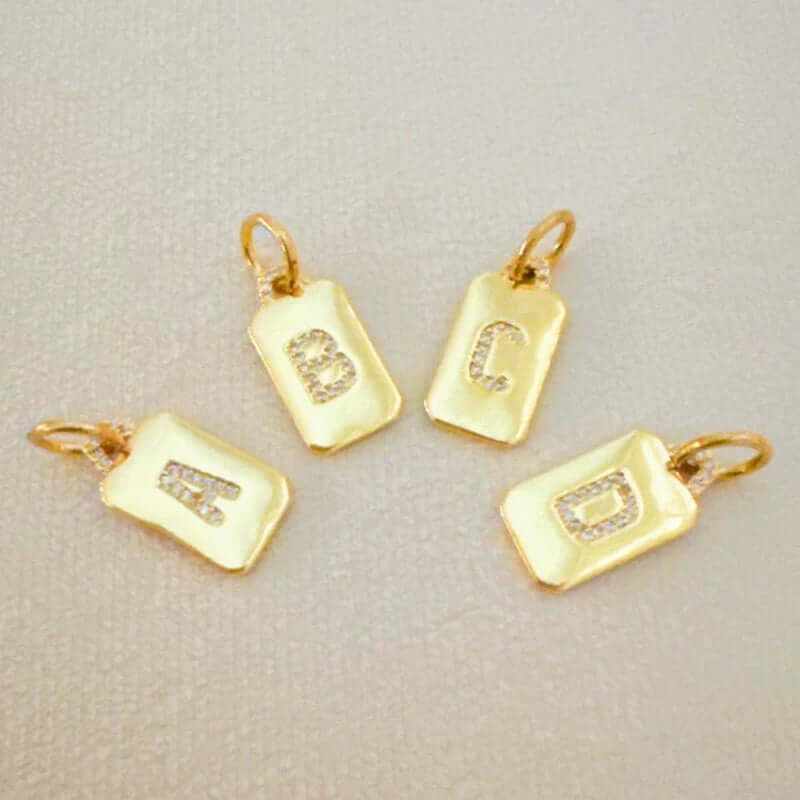 Four gold square initial charms with sparkling letters A, B, C, and D, ideal for personalized jewelry.