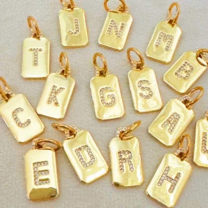 Gold personalized initial charms featuring sparkly letters on rectangular pendants for jewelry customization.