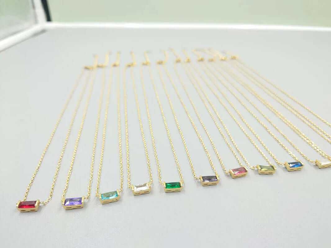 Row of 18K gold-plated baguette birthstone charm necklaces in vibrant colors