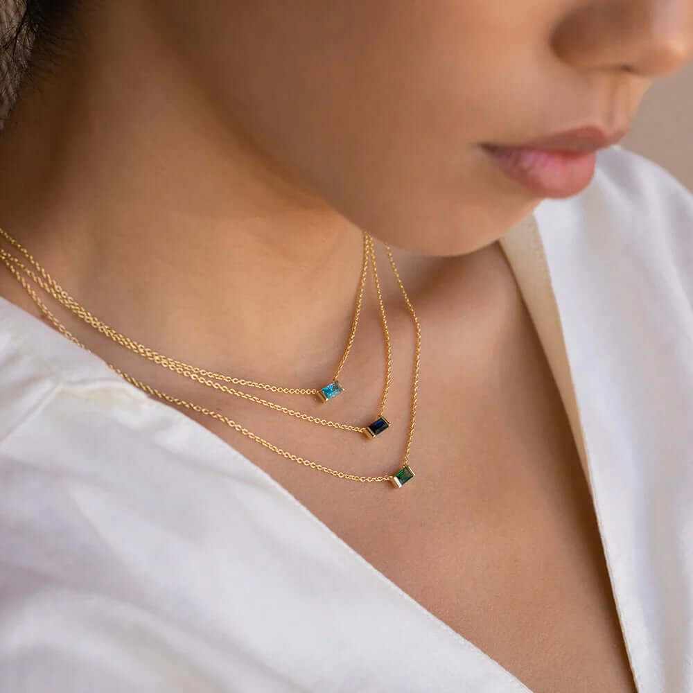 Model wearing a dainty 18K gold-plated baguette birthstone necklace with multiple layered chains.