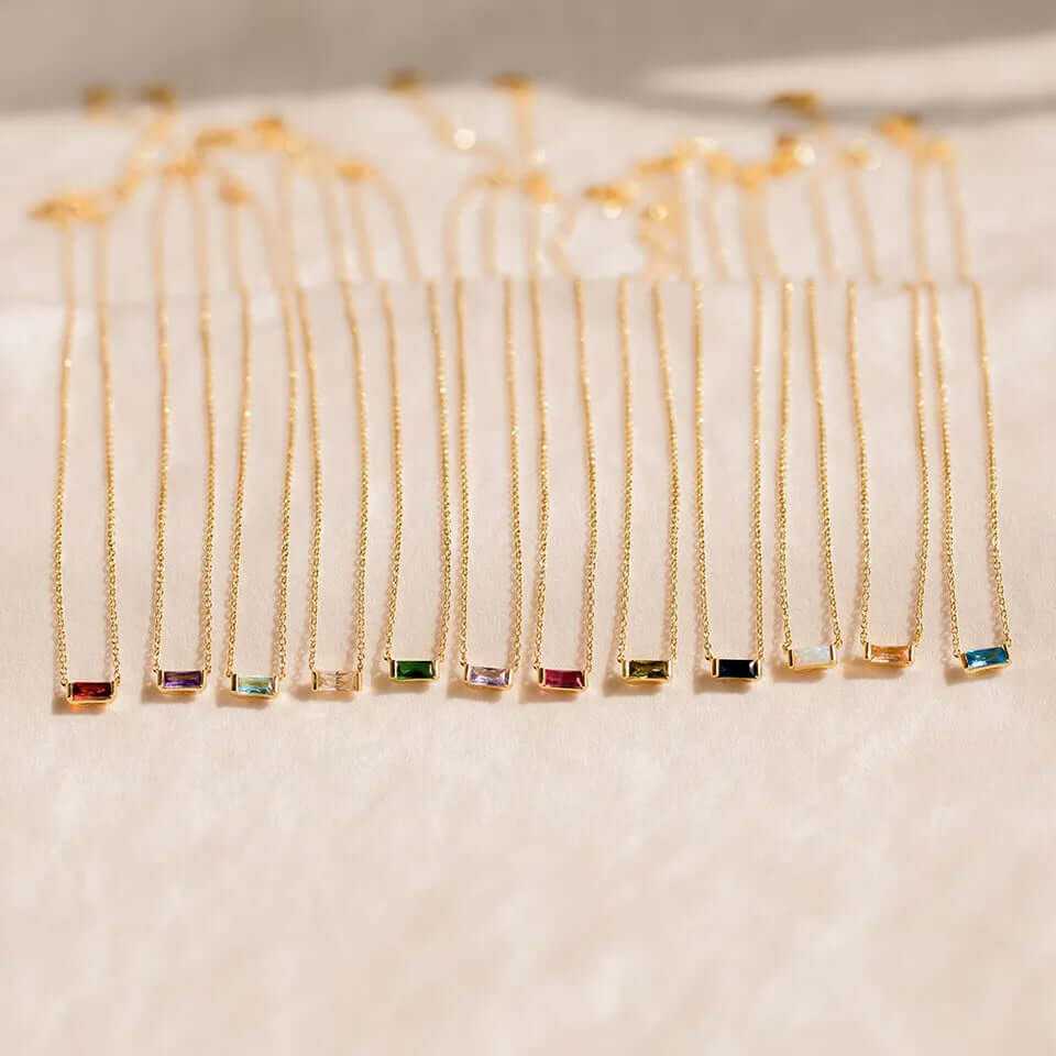 Dainty 18K Gold-Plated Baguette Birthstone Necklaces in a row, featuring various colored gemstones for each month.