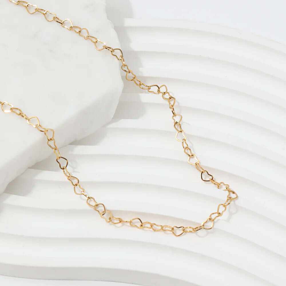 Dainty hollow heart choker necklace in gold-plated finish, elegantly displayed on a textured surface.