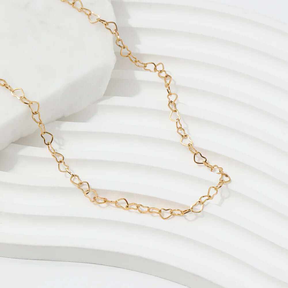 Dainty hollow heart choker necklace in gold-plated finish resting on a textured background.