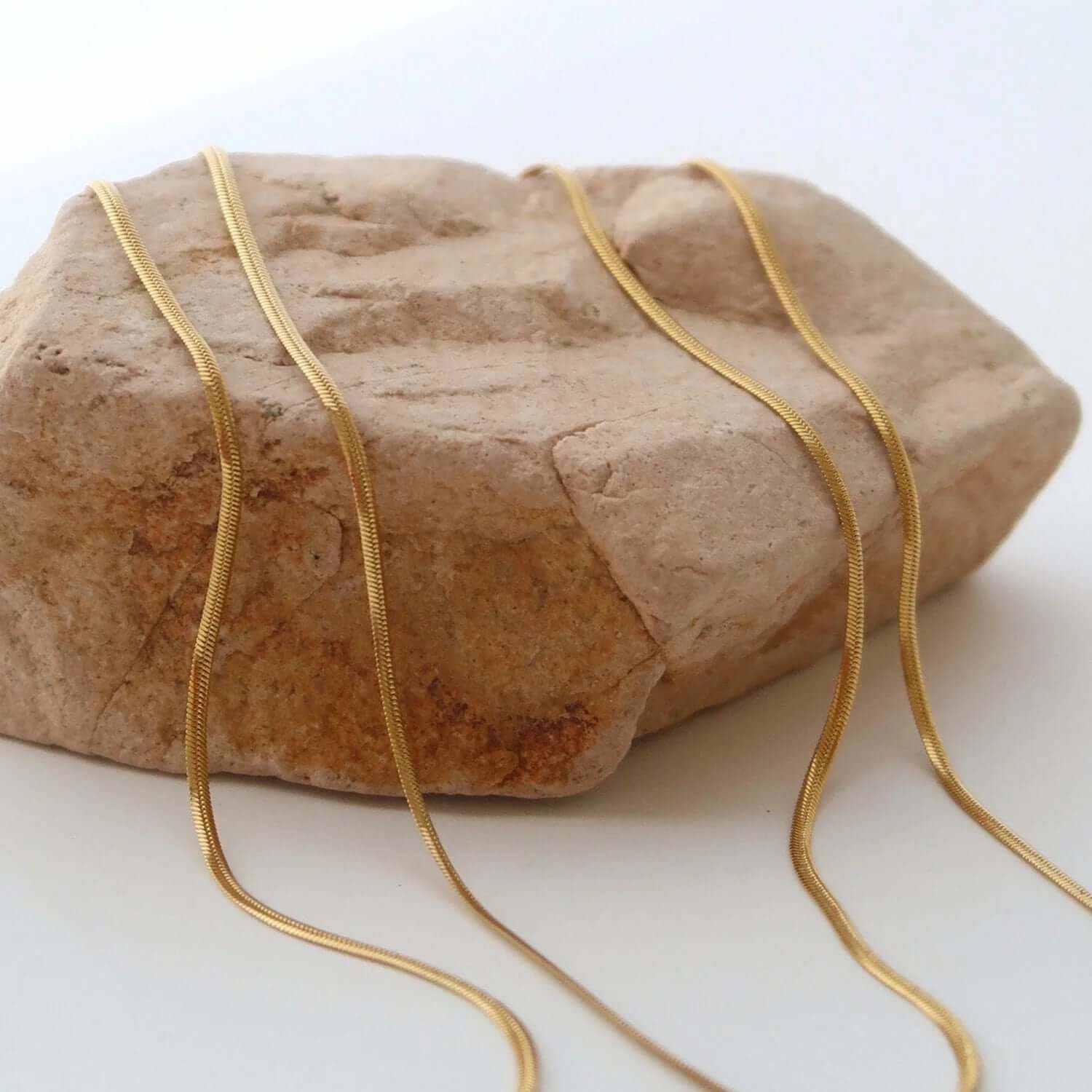 Layered gold plated choker necklaces displayed on a textured rock surface, showcasing elegant design and craftsmanship.