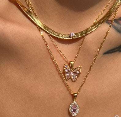 Close-up of layered gold necklaces featuring a butterfly pendant and pink zircon accents.