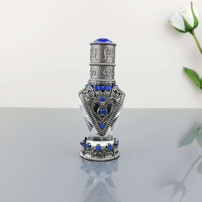 Decorative vintage cosmetic bottle with blue stones and intricate metal design on reflective surface