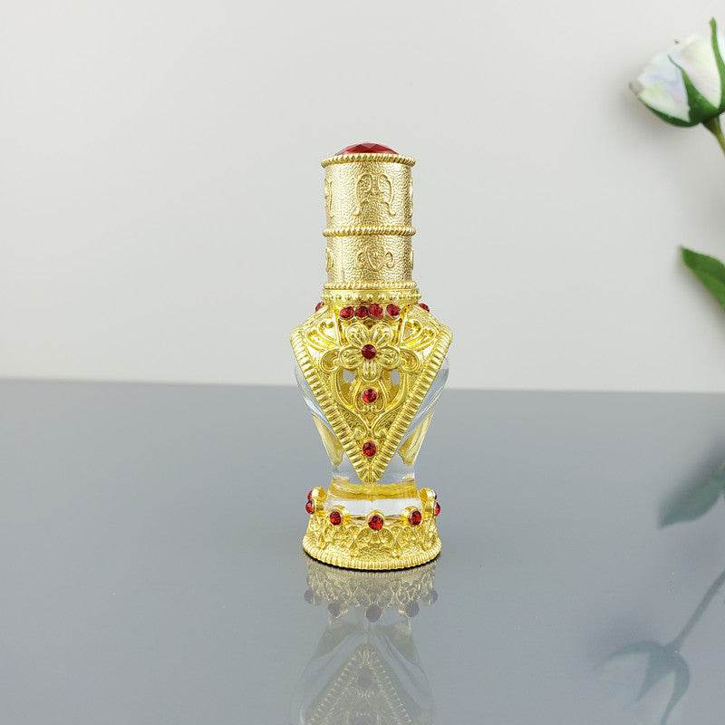 Gold decorative vintage cosmetic bottle with red stones and ornate design on reflective surface