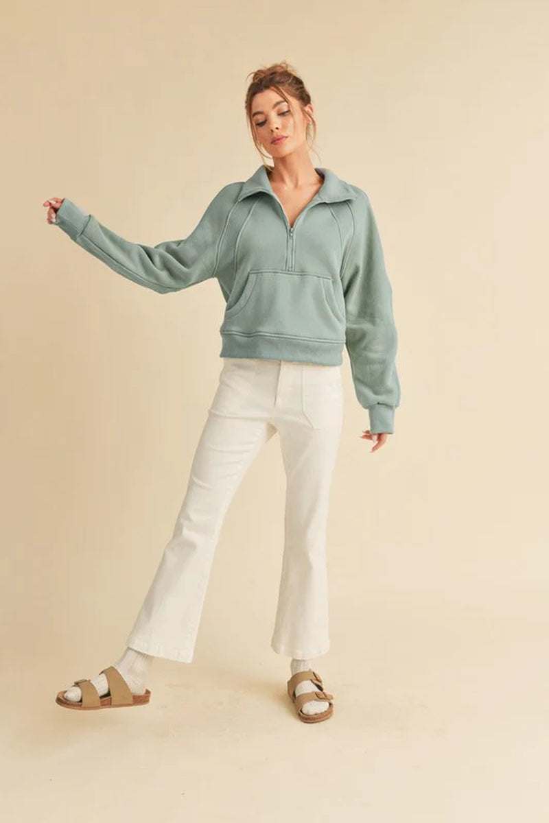 Model wearing Dove Funnel Neck Half Zip sweater paired with white flared jeans and sandals against a neutral background.
