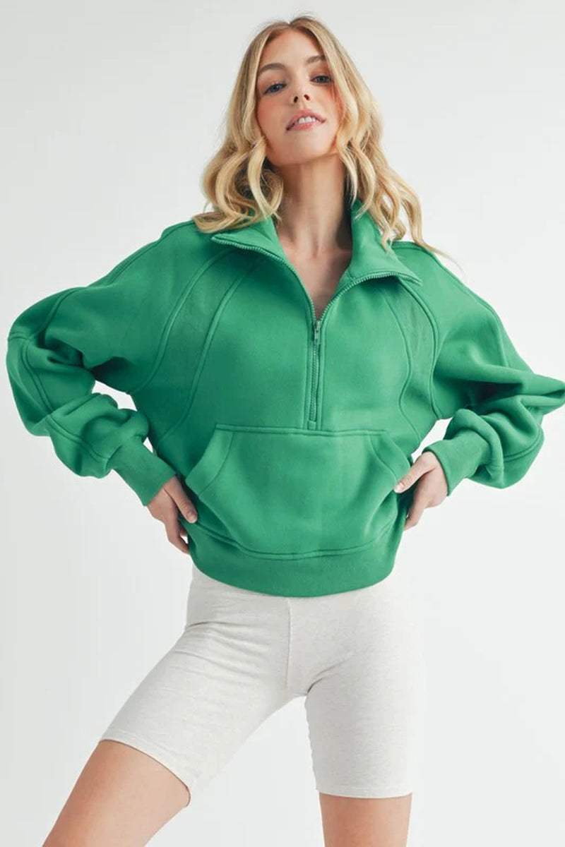 Woman modeling a green Dove half-zip sweater with oversized fit and cozy funnel neck, styled for comfort and relaxation.