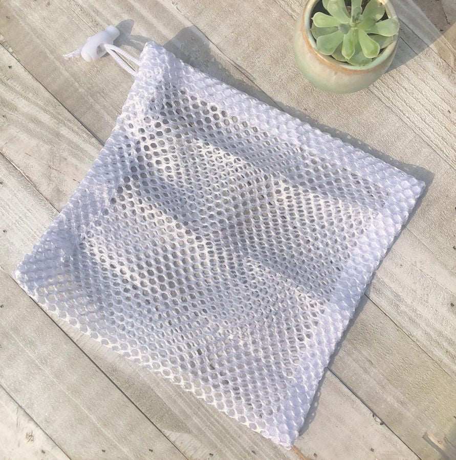 White mesh laundry bag on wooden surface with a small succulent plant, ideal for eco-friendly washing.