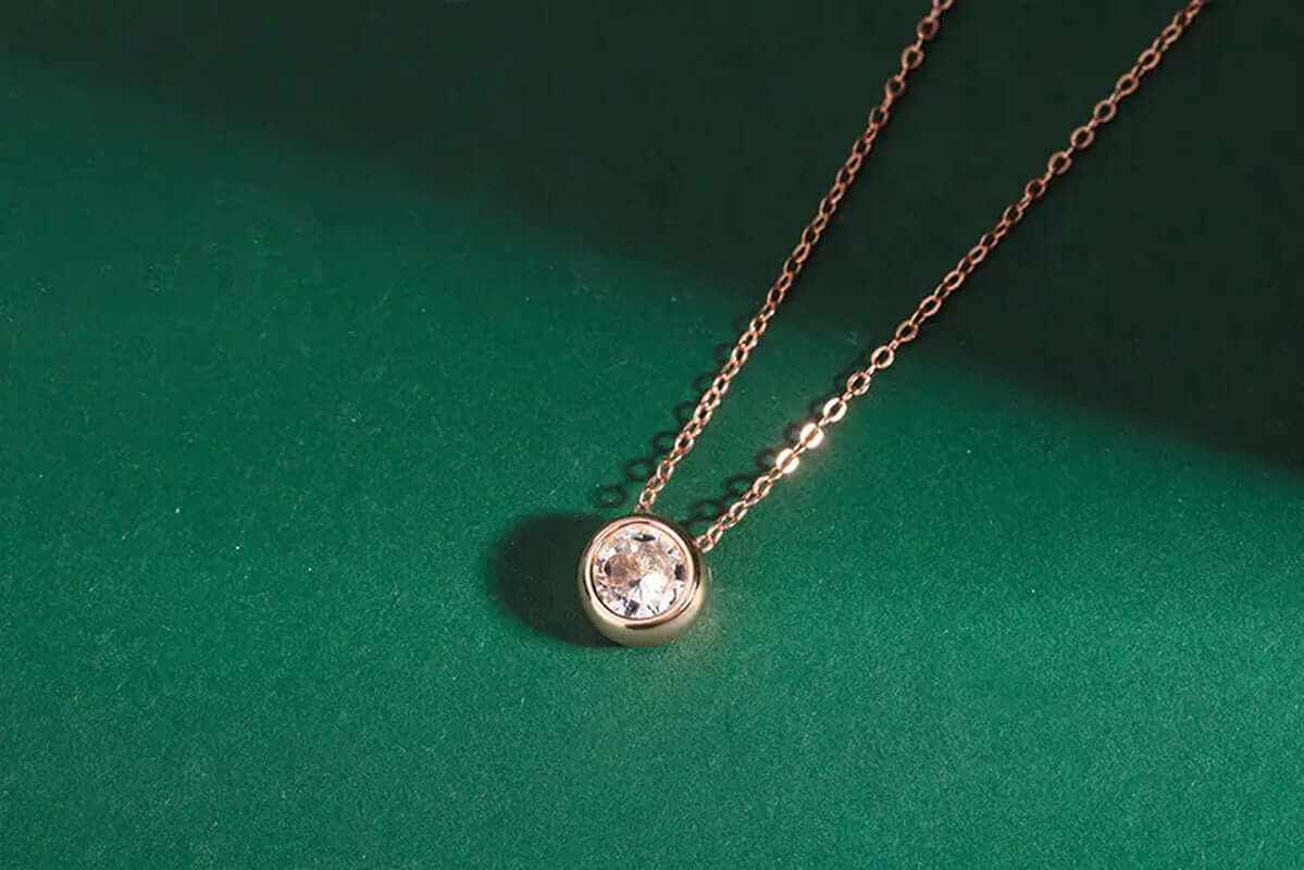 Rose gold choker necklace with round zircon pendant on a green background, showcasing elegance and charm.
