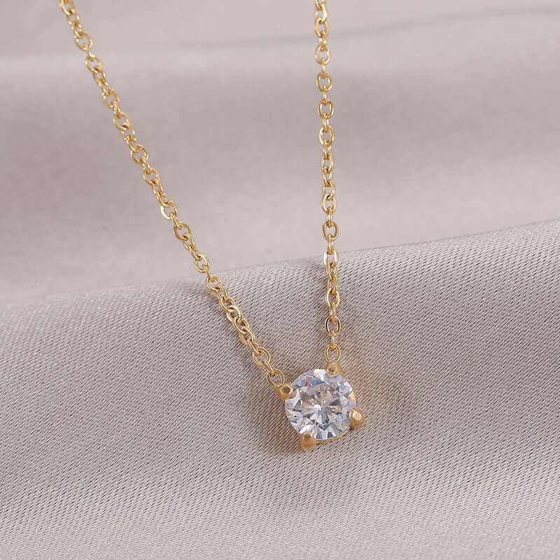 Elegant golden necklace featuring a round zircon birthstone pendant against a soft fabric background.
