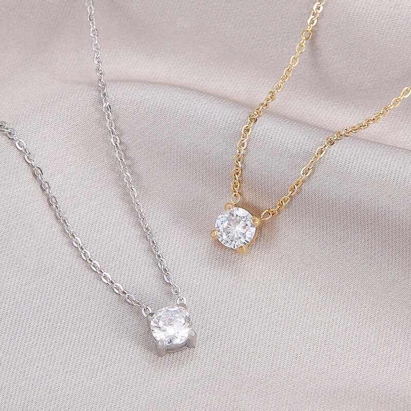 Elegant zircon birthstone necklaces in silver and gold settings on soft fabric backdrop.