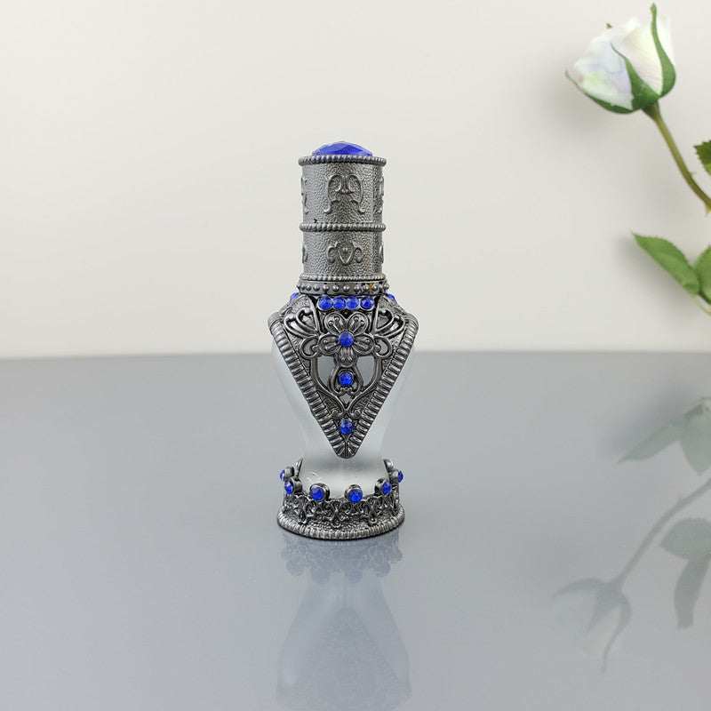 Decorative vintage cosmetic bottle with blue artificial stones and intricate alloy design on reflective surface