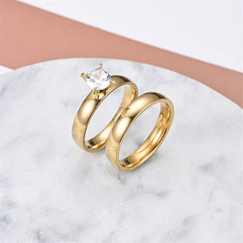 fashionable elegant stainless steel couple rings with gold plating and clear gemstone on marble background