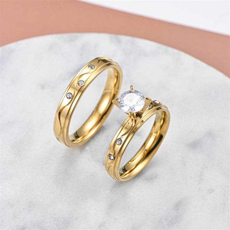 Fashionable elegant gold-tone stainless steel couple rings with embedded crystals on marble surface