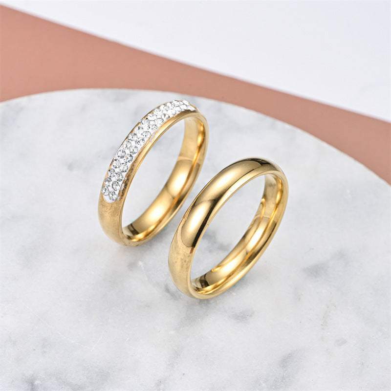 Fashionable elegant stainless steel gold couple rings with crystal accents on marble background