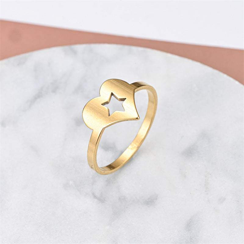 Fashionable elegant stainless steel gold-tone ring with heart and star cutout design on marble background