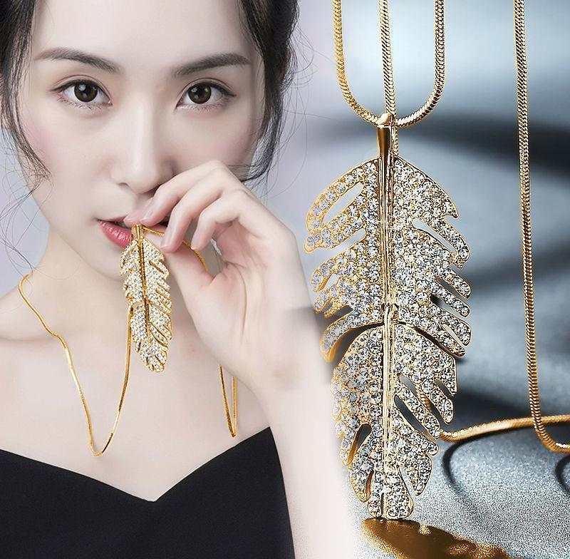 Fashionable layered long necklace with gold alloy feather pendant and rhinestones worn by woman