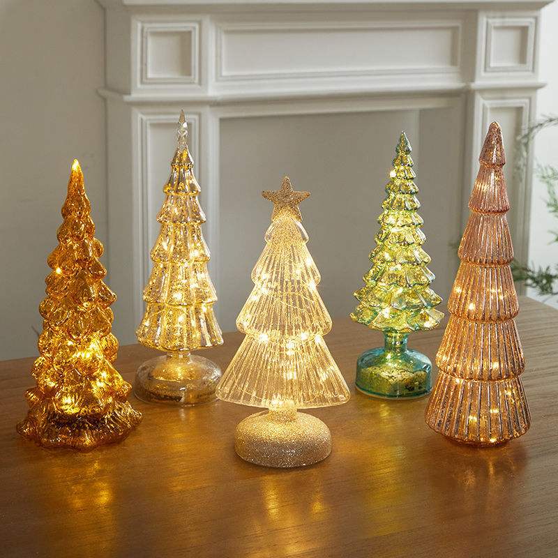 Christmas table decorations featuring illuminated glass Christmas trees in various colors and shapes.