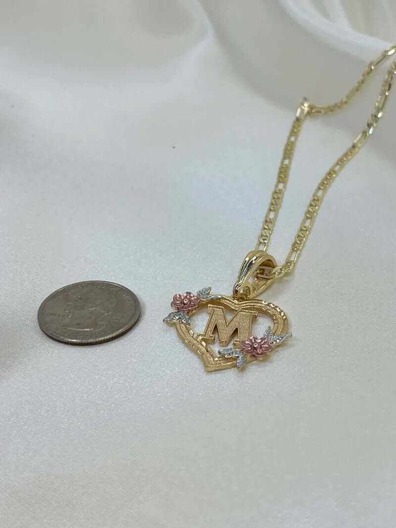 Gold plated heart shaped initial pendant necklace with floral details, featuring letter M, next to a quarter for size reference.