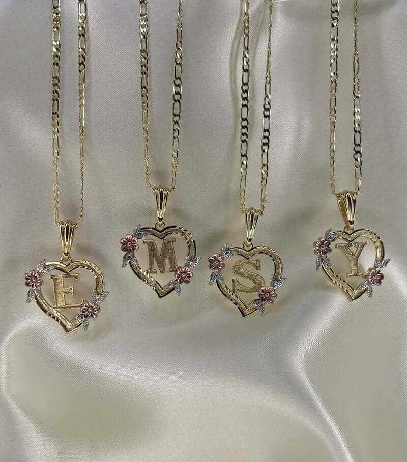 Gold plated heart-shaped initial pendant necklaces featuring letters E, M, S, Y adorned with roses on a silk background.