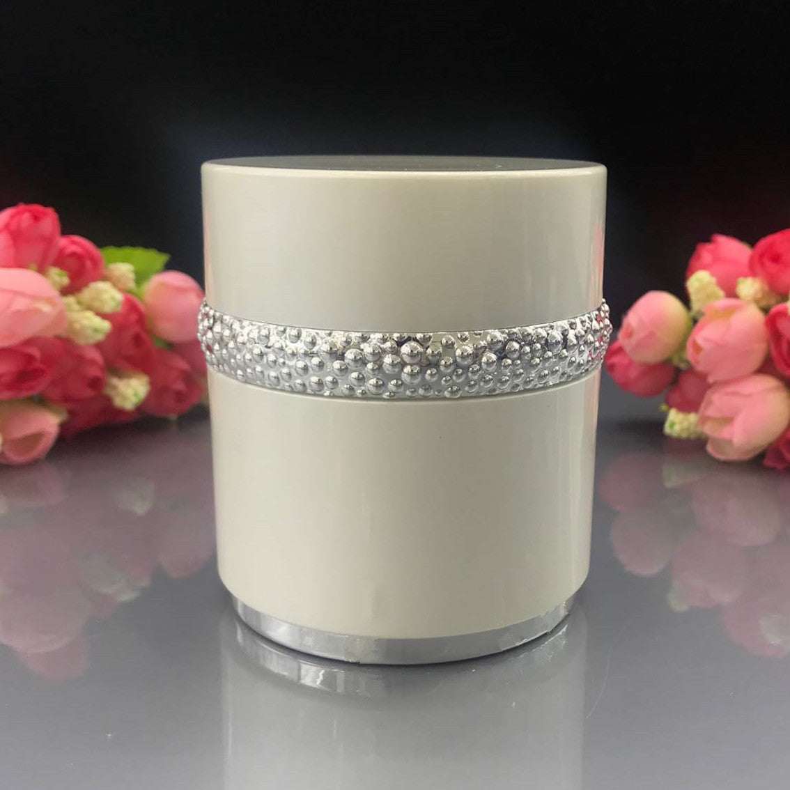 High-grade sub-bottling pearl set white cream container with rhinestone band and silver base on reflective surface with pink flowers background