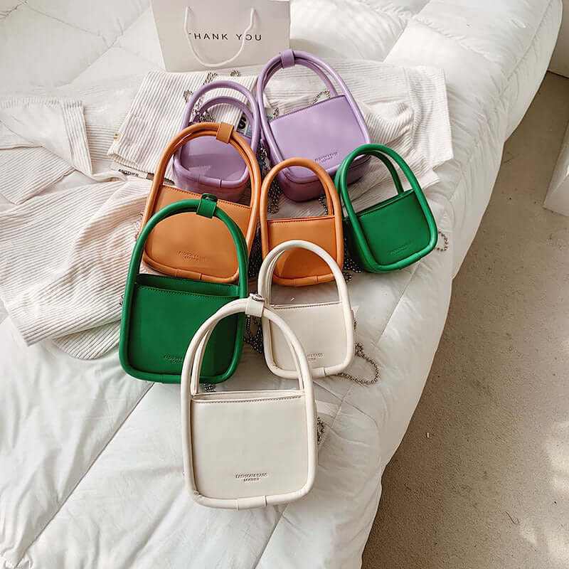 Collection of colorful women’s luxury designer mini chain handbags in various shades on a white fabric background