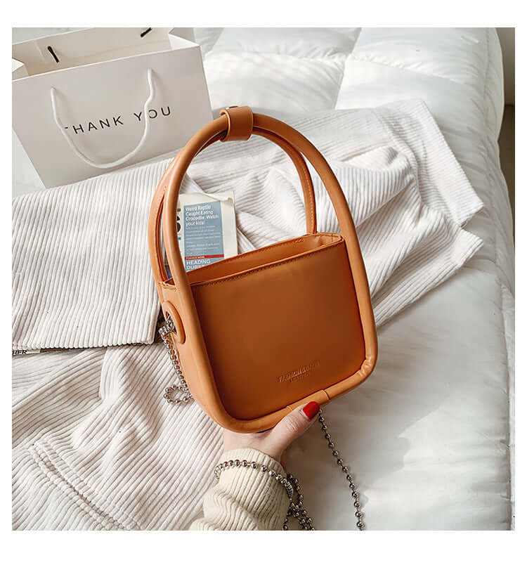 High quality women's luxury designer mini chain handbag in brown leather with chain handle on white textured fabric background