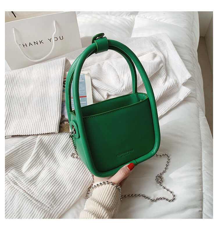 Green women's luxury designer mini chain handbag with silver chain handle on white fabric background