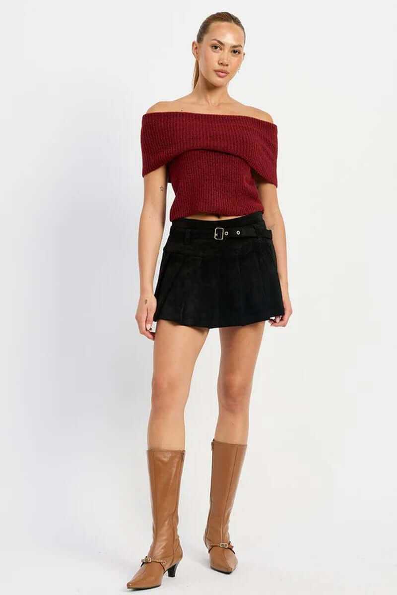 Model wearing a chic high-waisted pleated suede belted skort with an off-the-shoulder top and knee-high boots.