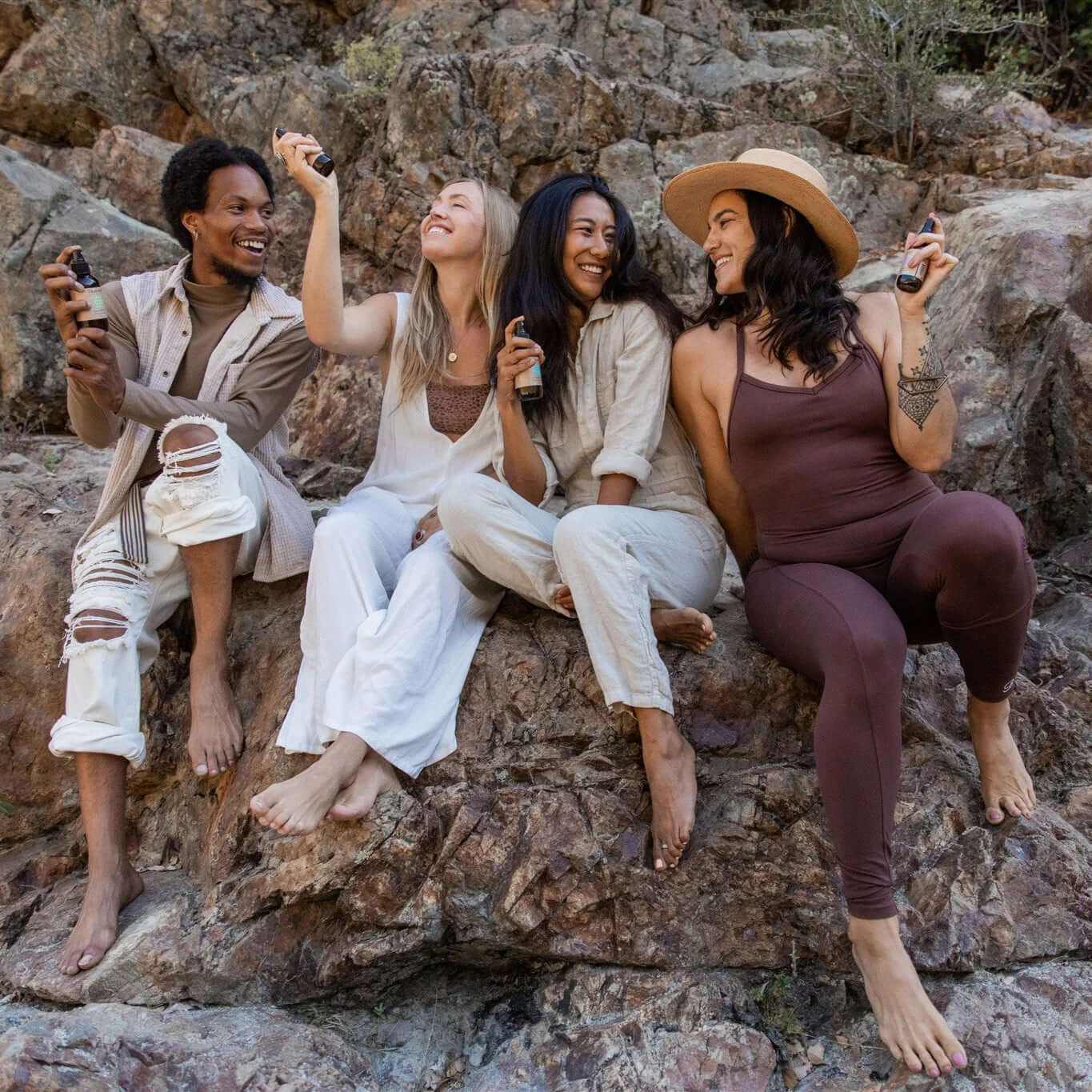 Four friends enjoying holistic aromatherapy mood spritzers while sitting on rocks outdoors.