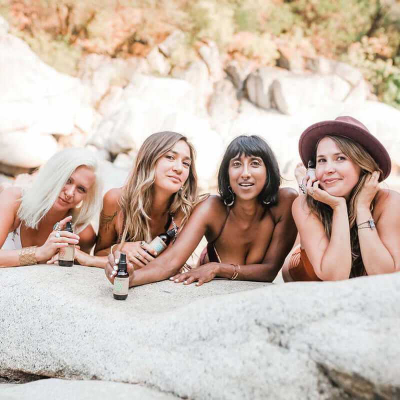 Four women enjoying Holistic Aromatherapy Ayurvedic Mood Spritzer Kit by a rocky outdoor setting.